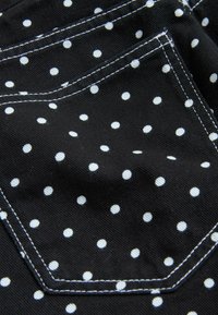 Sort stof med hvide polkaprikker, der har en syet lomme med synlige dobbelte hvide sømme.