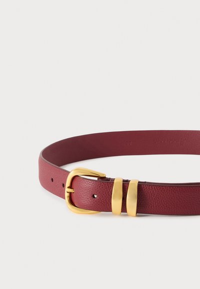 Ceinture en cuir rouge avec une boucle en métal doré et deux boucles dorées sur un fond blanc uni.