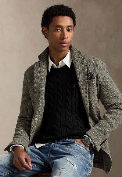 Vyriškas žuvies kaulo rašto švarkas pilkos ir baltos spalvos, dėvimas ant juodo megzto megztinio su pynėmis. Komplektuojamas su kontrastinga balta marškinėlių ir plačiam dėvėjimui skirtomis džinsais su dėvėjimo detalėmis.