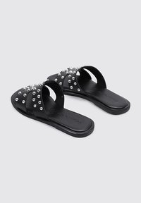 Chanclas negras de material sintético, con múltiples filas de tachuelas plateadas en la parte superior y suelas planas.