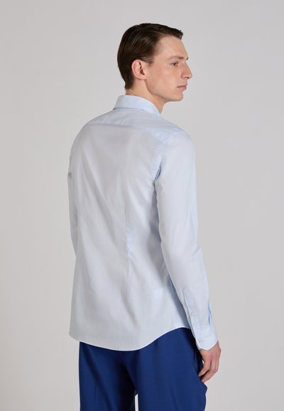 Camisa de manga larga azul claro hecha de algodón suave con cuello puntiagudo y puños con botones, con dobladillo curvado y costuras sutiles.