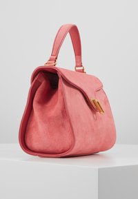 Sac à main en suède rose de forme structurée, avec une poignée supérieure et des accents en métal doré. Texture lisse et fermeture à rabat avec une légère courbure.