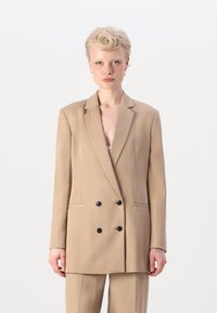 Beige dobbeltspent blazer med svarte knapper, klaffelapper og side lommer, laget av glatt stoff. Skreddersydd passform og lange ermer.