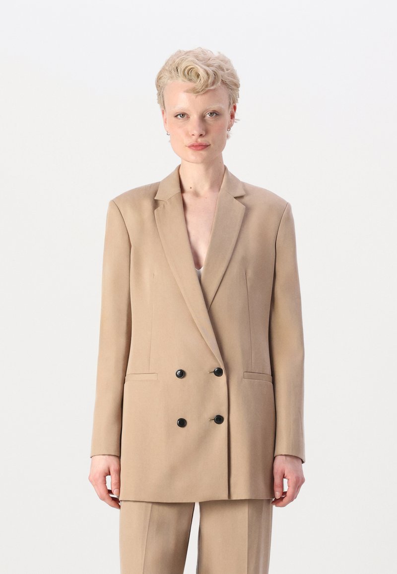 Beige dobbeltspent blazer med svarte knapper, klaffelapper og side lommer, laget av glatt stoff. Skreddersydd passform og lange ermer.