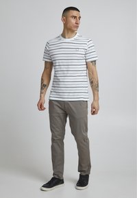 Hvit t-skjorte med korte ermer og marineblå horisontale striper, sammen med lys grå bukser og svarte joggesko.