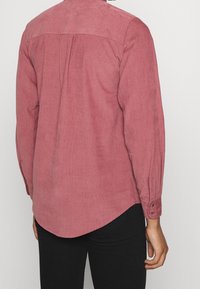 Langhals corduroy shirt in stofroze, met een rugschouder, knopenmanchetten en een ronde zoom. Zachte textuur met verticale ribbels.