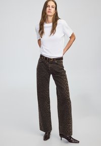 Spodnie w szerokim kroju w zwierzęcy wzór, w brązowo-czarnych odcieniach, zestawione z białą bluzką z krótkimi rękawami i ciemnym paskiem.