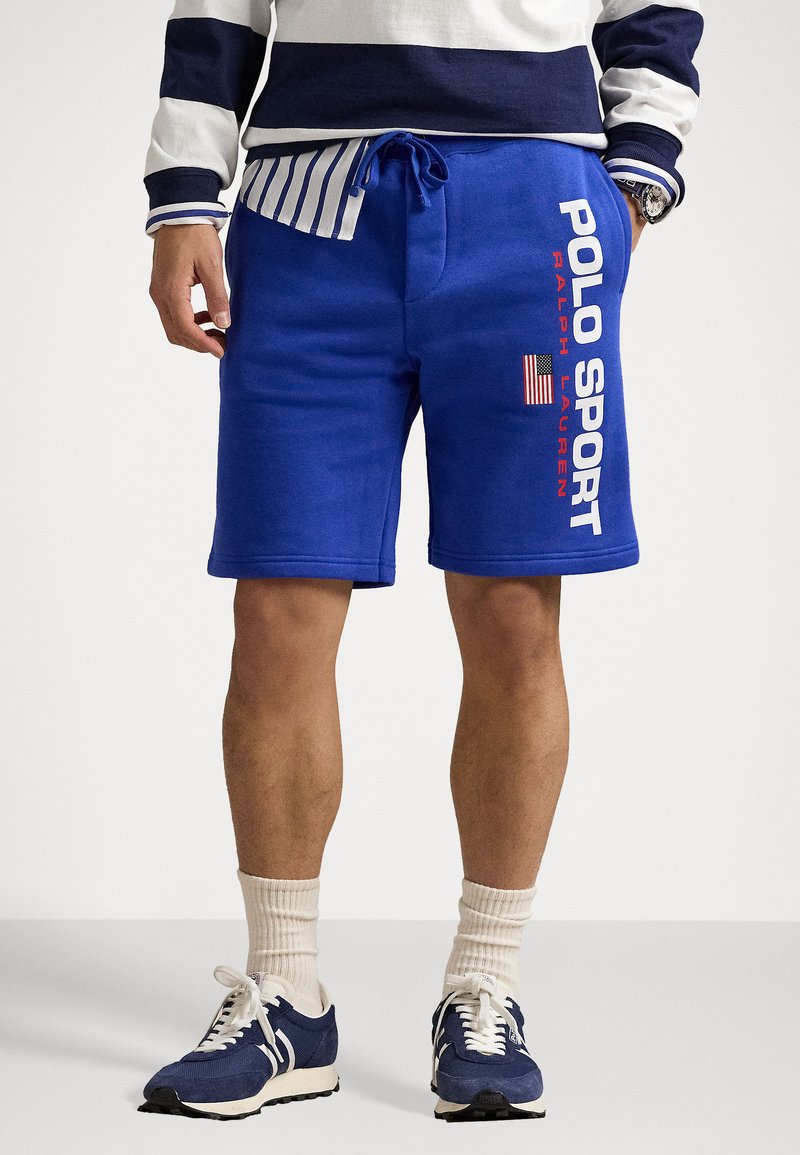 Mėlynos medvilninės šortai su raišteliu juosmenyje, ant kurių balta spalva užrašyta "POLO SPORT" ir maža Amerikos vėliavos detalė. Minimalistinis dizainas.