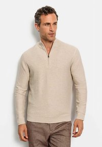 Maglione beige con mezza cerniera, dalla sottile texture a coste orizzontali, polsini aderenti e collo strutturato, abbinato a pantaloni marroni.