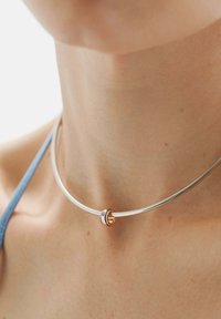 Collar de plata con un acento dorado liso y redondo con rayas azules. El diseño es elegante con una estética minimalista.