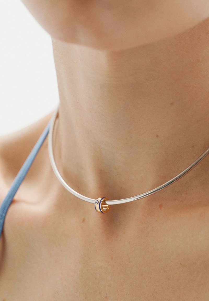 Collar de plata con un acento dorado liso y redondo con rayas azules. El diseño es elegante con una estética minimalista.