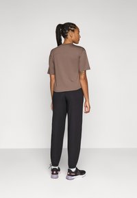 Brun kortärmad t-shirt, tillsammans med svarta löst sittande byxor och svarta sneakers. Diskret sömdetalj på t-shirten.