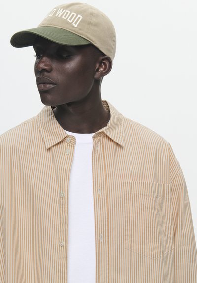 Casquette beige et olive avec broderie "WOOD WOOD" ; chemise à rayures en orange pâle et blanc, avec une poche poitrine.