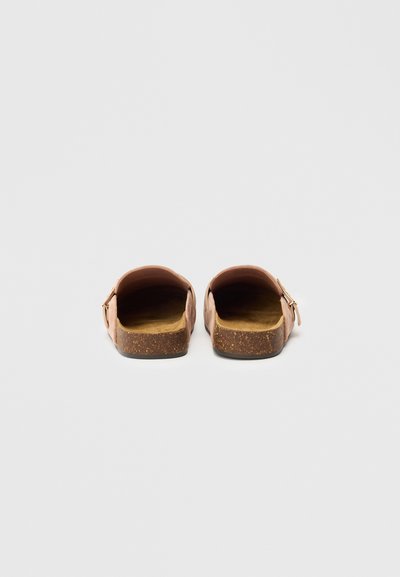 Roze natikače na slip-on z zglajenim zgornjim delom, oblikovanim plitvim plutastim podplatom in okroglo konico. Imajo minimalističen dizajn brez vidnih kovinskih delov.