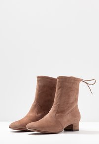 Bruna mockaskinnsankelskor med rund tå, låg blockklack och snördetalj baktill; slät textur och enkel design.