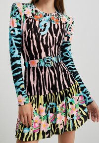 Robe colorée à manches longues présentant un mélange d'imprimés animaliers et de motifs floraux, avec un corsage ajusté, une jupe évasée et une ceinture assortie.