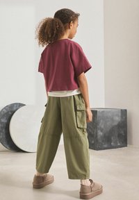 Kortärmad maroon crop top i kombination med lösa olivgröna cargo-byxor med sidofickor. Bruna skor med strukturerad yta.