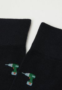 Marineblau Socken mit gerippter Textur, die auf jeder Seite ein grünes Drill-Motiv zeigen. Hergestellt aus einem weichen, elastischen Material für zusätzlichen Komfort.