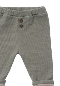 Hellgrüne Waffelstrick-Hosen mit weicher Textur, ausgestattet mit einem taillierten Bund und zwei braunen Knöpfen auf der Vorderseite.