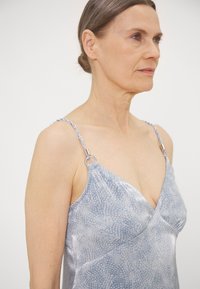 Silkkinen, vaalean sininen mekko, jossa on kukkakuosi, V-mallinen pääntie ja punotut olkaimet metallisilla yksityiskohdilla.