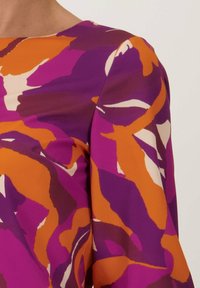 Kleurrijke blouse met een paars, oranje en witte abstracte print op een gladde stof. Het ontwerp heeft een ronde halslijn en lange mouwen.