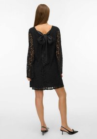 Mustast pitsist kleit pikkade varrukatega ja sügava V-kaelusega tagaküljel, kus on suur satiinist lips. Seelikuääres on peen pitsääris.