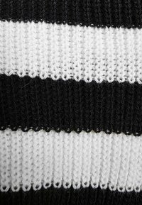 Dzianina z naprzemiennymi poziomymi paskami w kolorze czarnym i białym. Tekstura jest miękka, z widocznym pętelkowym, grubym splotem.