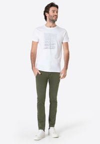White t-shirt with a graphic print, paired with olive green slim-fit pants and white sneakers. Casual outfit with simple design elements.