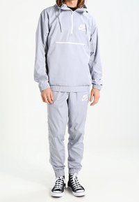 Lichtgrijze Nike pullover hoodie met een halve rits, verstelbare capuchon en zak; gecombineerd met bijpassende joggers en zwarte hoge sneakers.