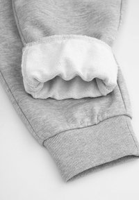 Szare bawełniane spodnie dresowe z ściągaczem na kostce i teksturowaną białą podszewką przy ściągaczu. Charakteryzują się gładką, miękką teksturą.