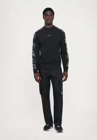 Sweatshirt preto com mangas padronizadas, gola redonda e logo. Combinado com calças de cargo pretas com bolsos laterais e marcação.