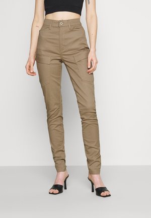 Khakifarbene Cargo-Hose mit hoher Taille, die über frontale Taschen und ein tailliertes Design verfügt. Hergestellt aus weichem Stoff und kombiniert mit eleganten schwarzen Absätzen.