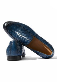 Zapatos de piel trenzada azul de tipo slip-on, con puntera redondeada, tacón bajo y textura suave. Costuras sutiles visibles.
