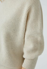 Hellbeige gestrickter Pullover mit strukturiertem Rippmuster, locker sitzend und mit Dreiviertelärmeln. Der Stoff wirkt weich und gemütlich.