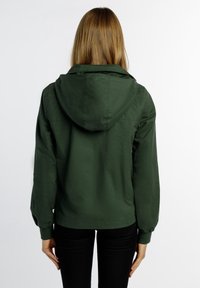 Veste à capuche verte en tissu léger, dotée de poignets élastiques et d'une coupe décontractée. Texture lisse avec un design simple.