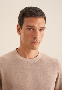 Maglione lavorato a maglia beige con scollatura rotonda, tessuto testurizzato, costine sottili sui polsini e sul fondo, e design minimalista.