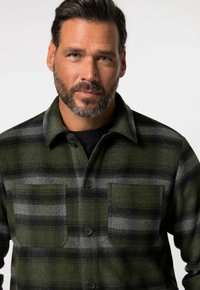 Camisa de franela a cuadros en verde y gris con dos bolsillos en el pecho, botones negros y un cuello; tejido texturizado con una apariencia suave y cálida.