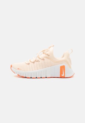 Nike sneaker featuring a pale peach mesh upper, white midsole with orange accents, ribbed sole, and textured heel support.
