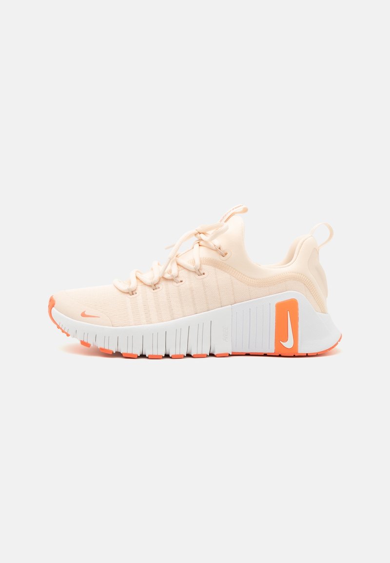 Sneakers Nike z jasnopomarańczową siateczką, białą podeszwą środkową z pomarańczowymi akcentami, żebrowaną podeszwą i teksturowanym wsparciem pięty.