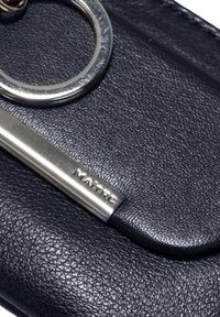 Črn teksturiran usnjeni izdelek s srebrnim kovinskim obodom in srebrnim logotipom. Ima gladek rob in subtilne detajle.