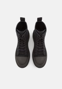 Sneakers alte nere con tomaia in tela testurizzata, punta tondeggiante, suola in gomma e lacci tono su tono. Linguetta tattili sul tallone per un facile indossamento.