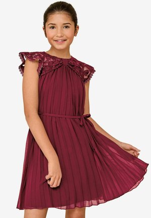 Burgundy pleatattu mekko, jossa on pitsiset hihansuut ja pyöreä pääntie. Mekossa on yhteensopiva vyö vyötäröllä ja liehuva, kevytrakenteinen kangas.