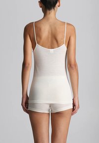 Camisola bianca in cotone con sottili spalline, design aderente e texture liscia. Indossata con mutandine coordinate, che mostrano uno stile minimalista.