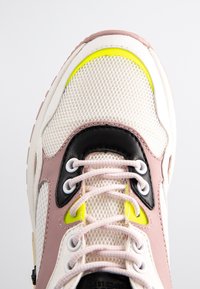 Sko med ett lätt beige nätövre, rosa och svarta överlägg, gula accenter och vit snörning. Tjock gummisula som ökar hållbarheten.