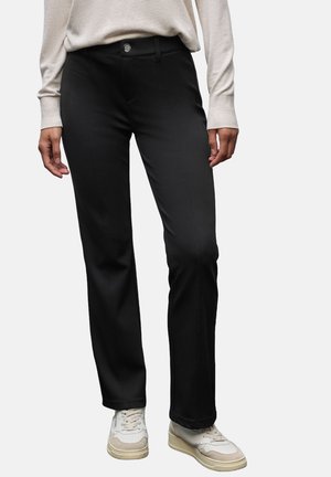 Schwarze Hose aus glattem Stoff mit geradem Bein und einer vorderen Knopfleiste. Kombiniert mit hellen Sneakers.