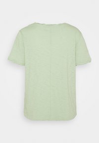 Camiseta de color verde claro de manga corta vista desde la parte trasera, con una costura vertical central y una tela casual, ligeramente texturizada.