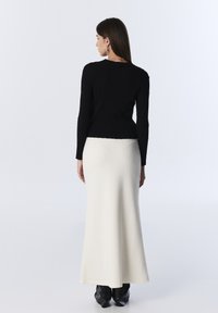 Zwarte geribbelde lange mouw top gecombineerd met een witte maxi rok, met een fitted ontwerp en een gestructureerde stof, gedragen met zwarte kniehoge laarzen.