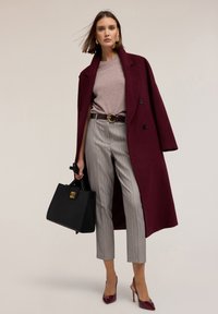 Burgundský vlněný kabát, světle fialový svetr, šedé pruhované kalhoty, černá kabelka se zlatými detaily a lesklé burgundské lodičky.