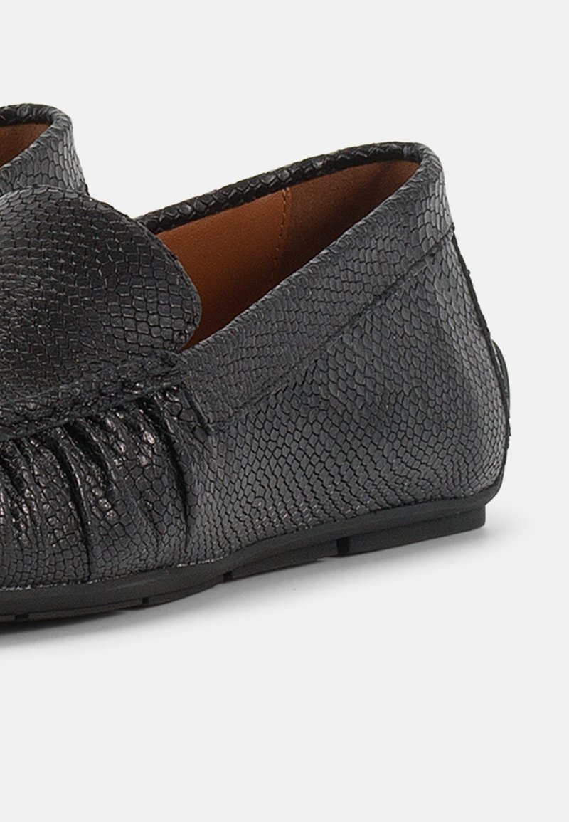 Schwarzer Lederloafer mit strukturiertem Muster, gerafftem Seitendetail und braunem Innenfutter, von der Seite vor weißem Hintergrund gezeigt.