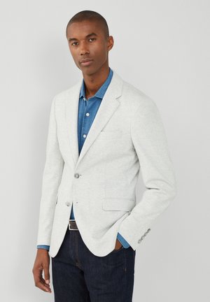 Hellgrauer Blazer aus weichem Stoff, mit einer Zwei-Knopf-Front, Reverskragen und zwei vorderen Taschen. Trägt man über einem Jeanshemd.